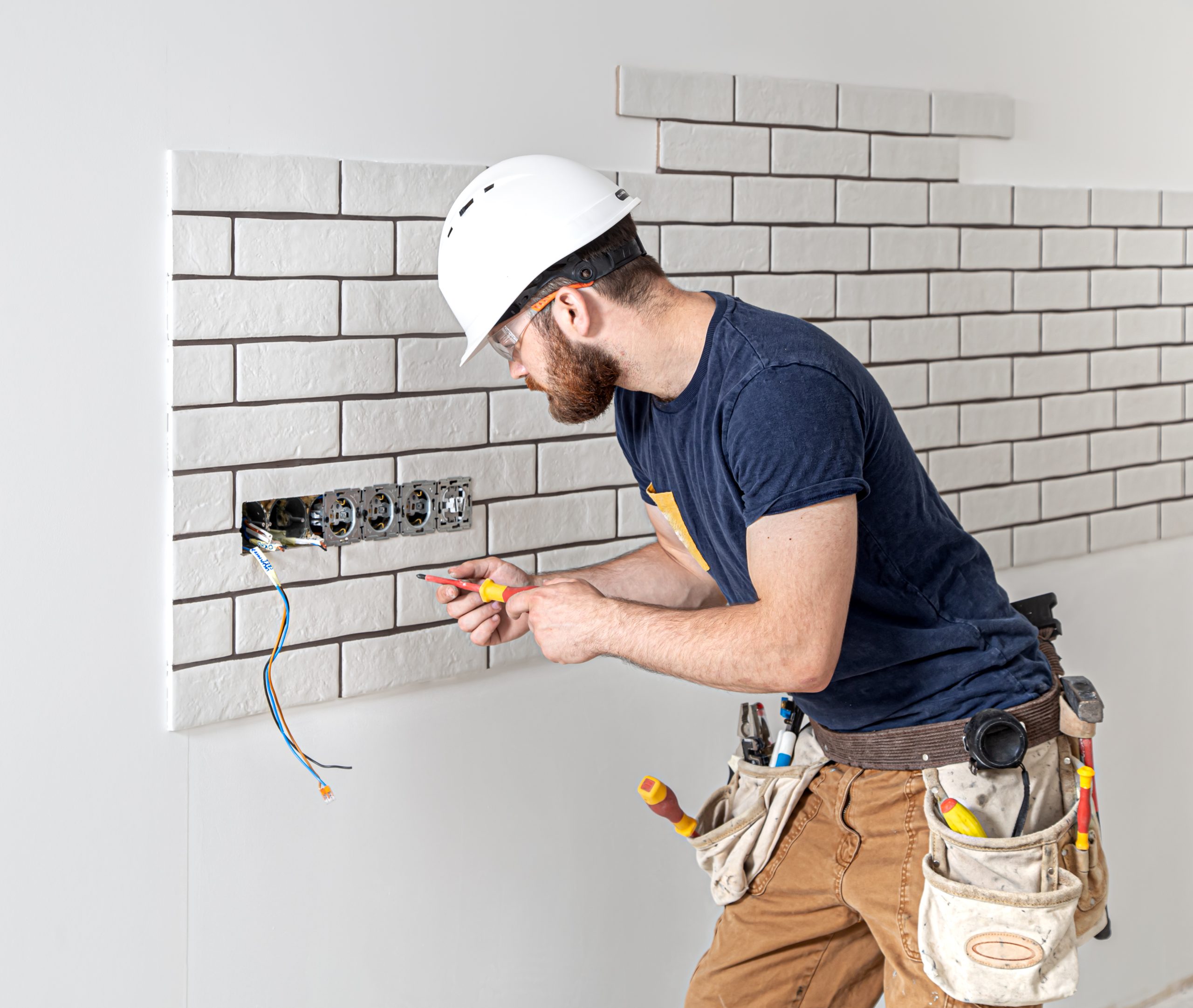 Electrician builder in a white helmet at work, installation of sockets, and switches